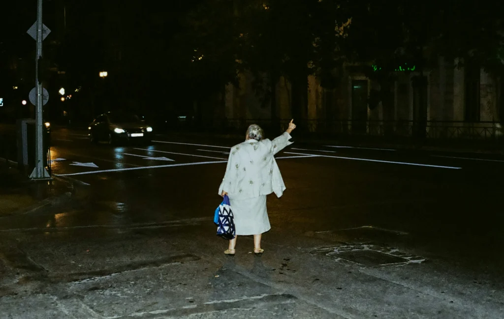 An old woman is hitchhiking in the dark